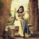 South Asian woman reading a book on a bench in a serene outdoor park setting.